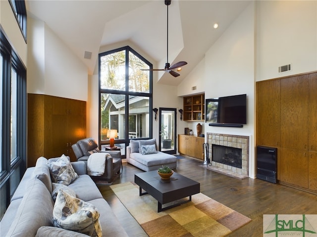 living room featuring wooden walls, dark hardwood / wood-style floors, a tiled fireplace, and high vaulted ceiling