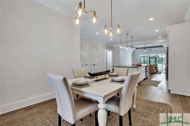 dining space with ornamental molding, light wood-type flooring, and ceiling fan with notable chandelier