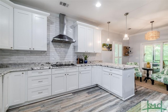 kitchen featuring kitchen peninsula, wall chimney exhaust hood, tasteful backsplash, decorative light fixtures, and white cabinetry