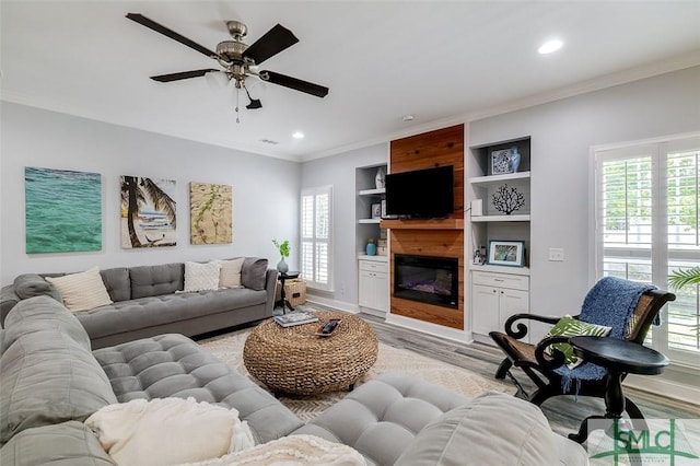 living room featuring built in shelves, light wood-type flooring, a large fireplace, and ceiling fan