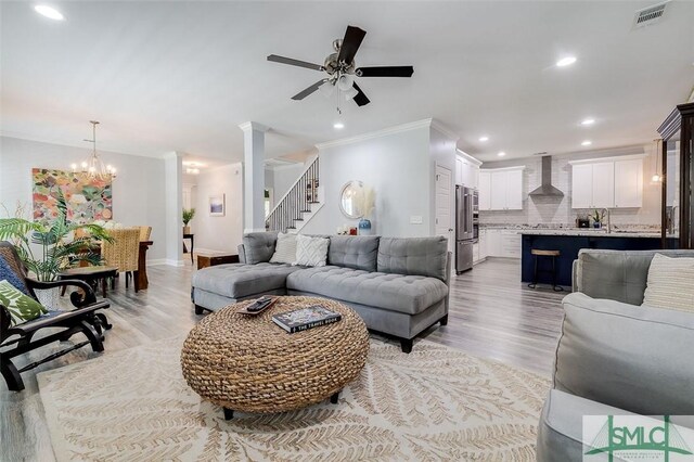 living room with ceiling fan with notable chandelier, light wood-type flooring, and ornamental molding