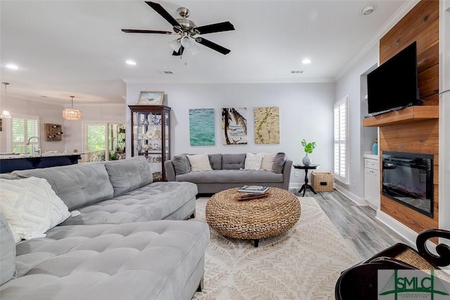 living room featuring ceiling fan with notable chandelier, light hardwood / wood-style floors, ornamental molding, and sink