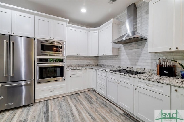 kitchen featuring light stone countertops, wall chimney exhaust hood, stainless steel appliances, white cabinets, and light wood-type flooring