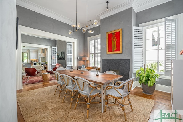 dining area with a healthy amount of sunlight, light wood-type flooring, crown molding, and an inviting chandelier