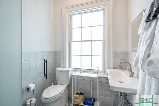 bathroom with toilet, sink, and tile walls