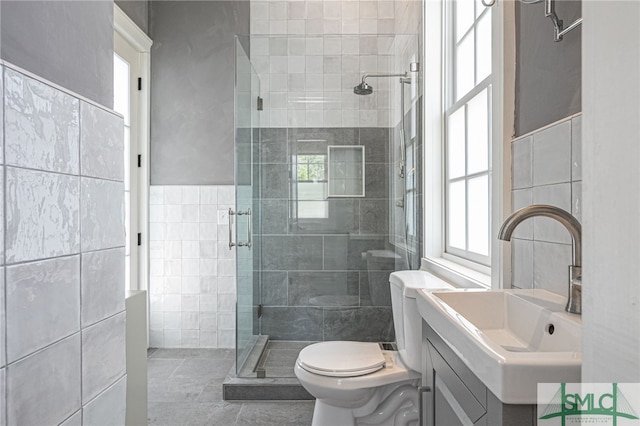 bathroom with vanity, a shower with door, tile patterned flooring, toilet, and tile walls