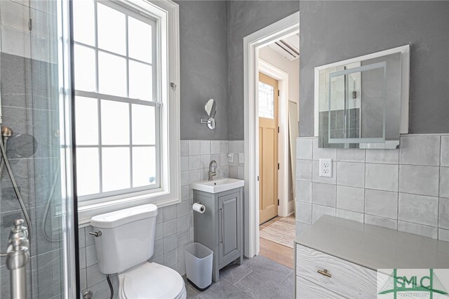 bathroom featuring tile patterned floors, vanity, tile walls, toilet, and a shower with shower door