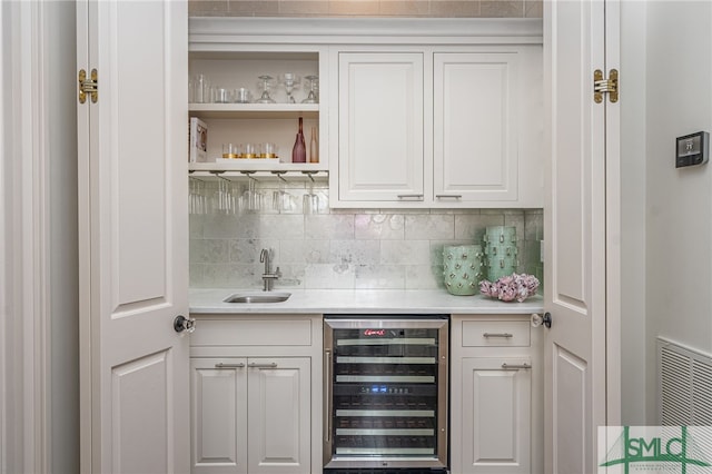 bar featuring tasteful backsplash, wine cooler, white cabinetry, and sink