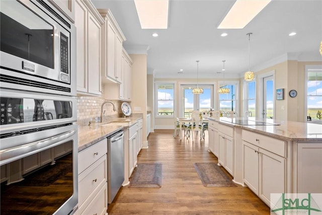 kitchen featuring crown molding, appliances with stainless steel finishes, a center island, light stone counters, and decorative light fixtures