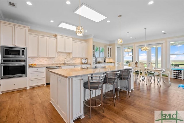 kitchen featuring appliances with stainless steel finishes, decorative light fixtures, a breakfast bar area, a large island, and crown molding