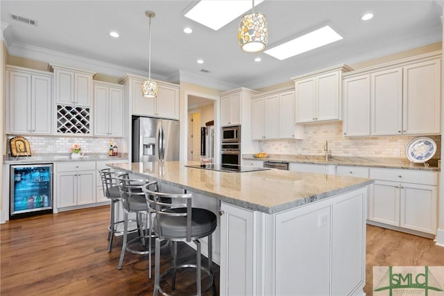 kitchen with stainless steel appliances, a kitchen island, beverage cooler, and decorative light fixtures