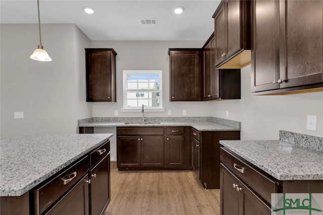 kitchen featuring light hardwood / wood-style flooring, dark brown cabinetry, light stone counters, hanging light fixtures, and sink