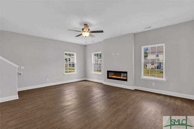 unfurnished living room featuring dark wood-style floors, baseboards, a ceiling fan, and a glass covered fireplace