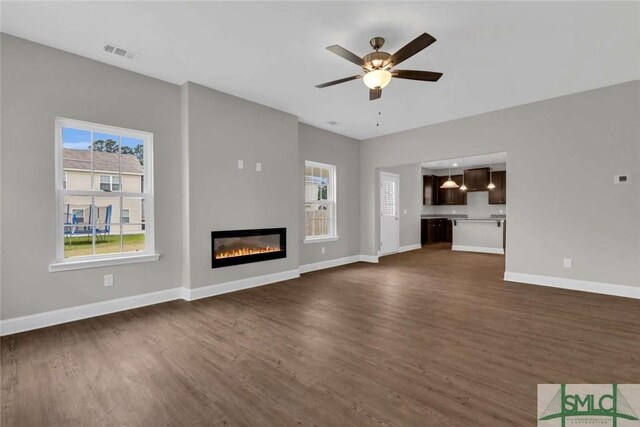 unfurnished living room with visible vents, dark wood-type flooring, a glass covered fireplace, a ceiling fan, and baseboards