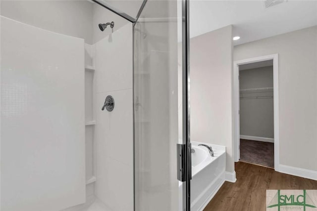 full bathroom featuring a walk in closet, a garden tub, a stall shower, wood finished floors, and baseboards