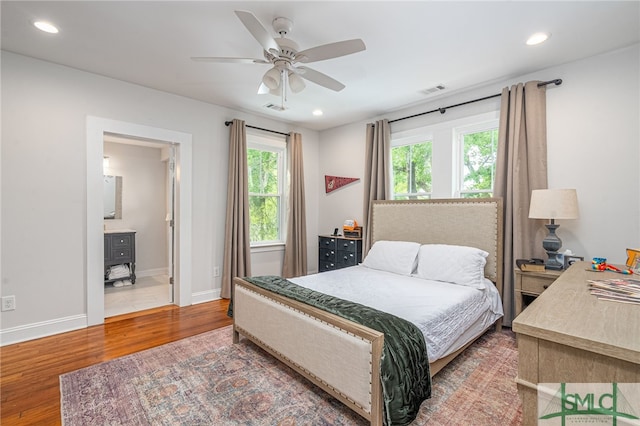 bedroom featuring connected bathroom, ceiling fan, multiple windows, and hardwood / wood-style flooring