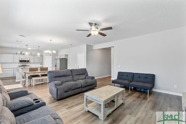 living room featuring a textured ceiling, light wood-type flooring, and ceiling fan with notable chandelier