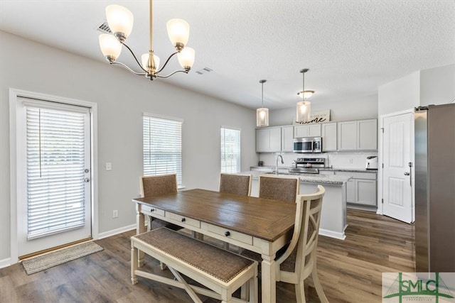 dining room with a notable chandelier, sink, a textured ceiling, and dark wood-type flooring