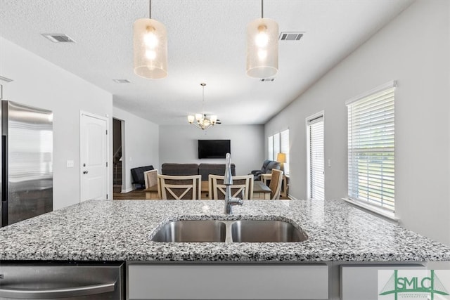 kitchen with stainless steel appliances, decorative light fixtures, and a kitchen island with sink