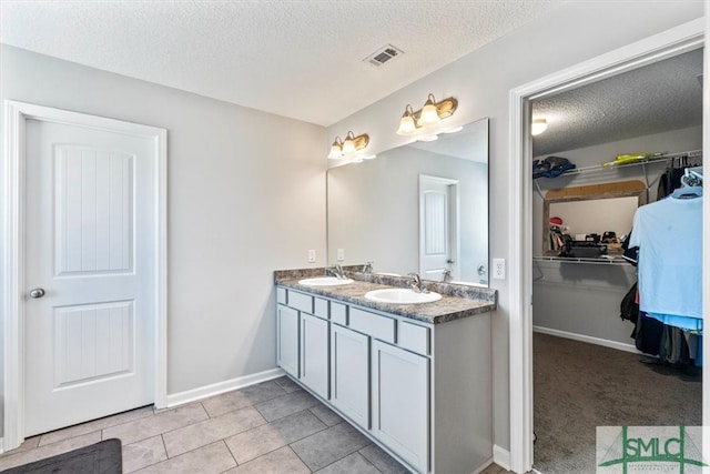 bathroom with tile flooring, a textured ceiling, and dual bowl vanity