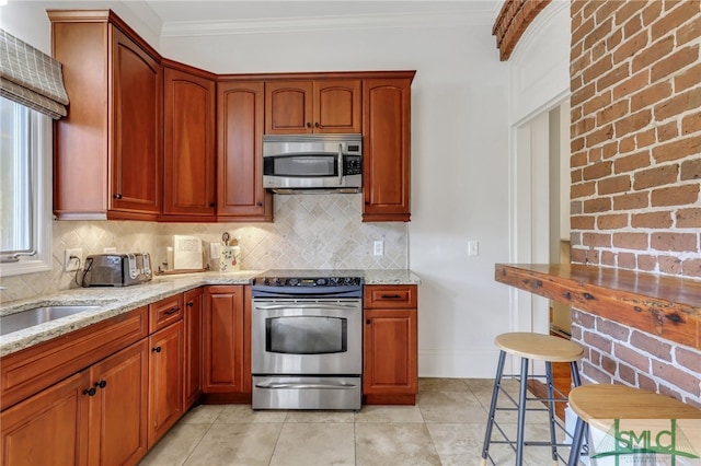 kitchen featuring appliances with stainless steel finishes, light stone counters, crown molding, and decorative backsplash