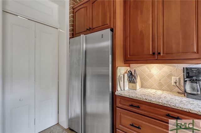 kitchen featuring light stone countertops, tasteful backsplash, and stainless steel refrigerator