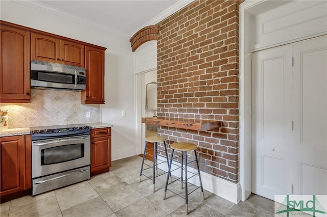 kitchen featuring tasteful backsplash, crown molding, light stone countertops, light tile patterned floors, and stainless steel appliances