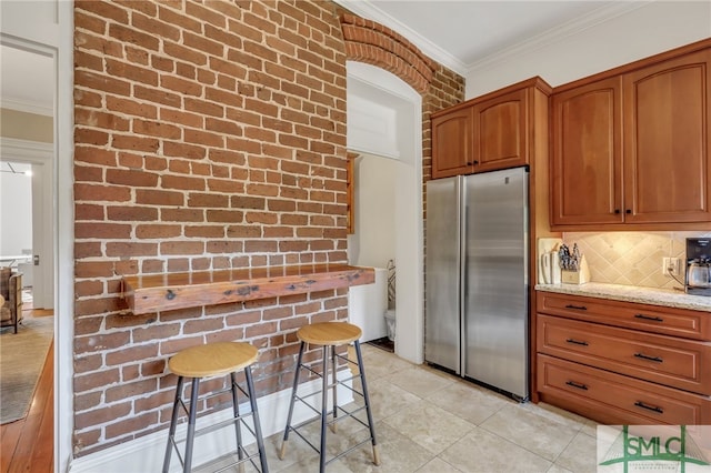 kitchen with decorative backsplash, light stone countertops, crown molding, and stainless steel refrigerator