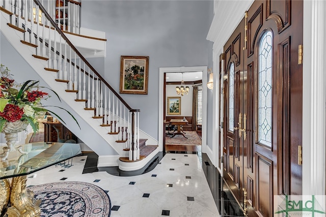 entryway with a towering ceiling, tile flooring, crown molding, and a chandelier