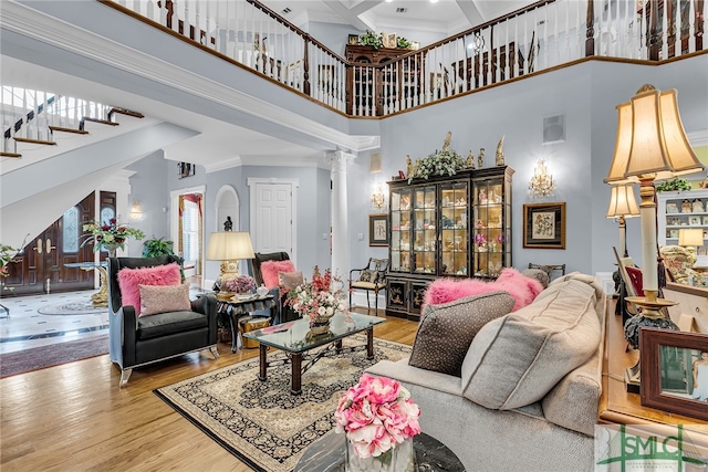 living room featuring wood-type flooring, a high ceiling, decorative columns, and crown molding