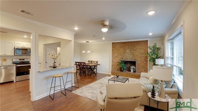 living room with a fireplace, wood finished floors, visible vents, and crown molding