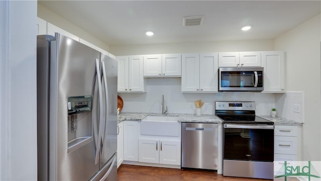 kitchen with visible vents, appliances with stainless steel finishes, light stone countertops, white cabinetry, and a sink