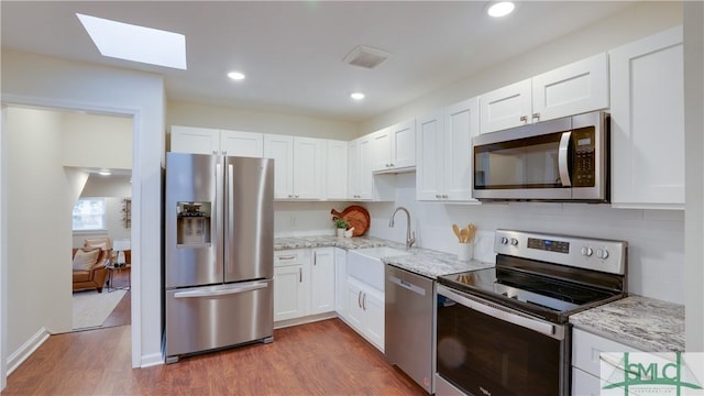 kitchen with wood finished floors, a sink, white cabinets, appliances with stainless steel finishes, and light stone countertops