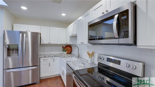 kitchen with appliances with stainless steel finishes, white cabinets, a sink, and light stone counters