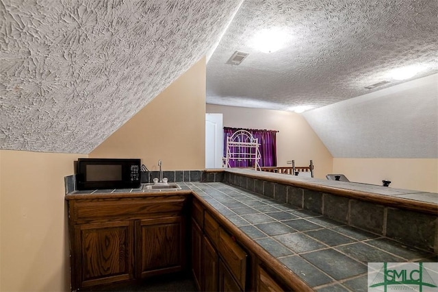 bar with a textured ceiling, vaulted ceiling, tile counters, and sink