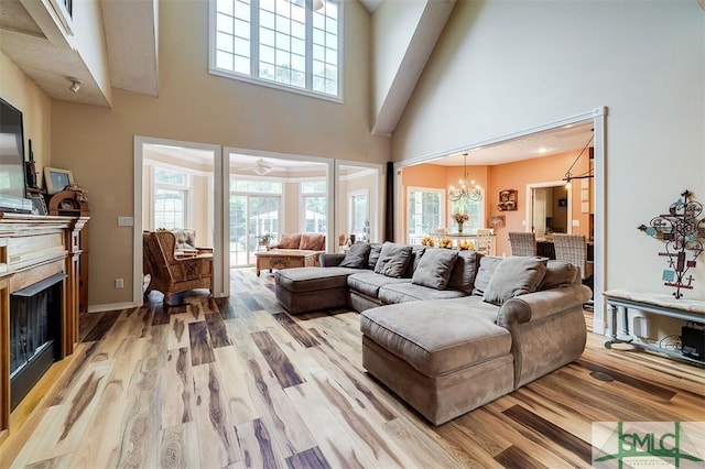 living room with ceiling fan with notable chandelier, a towering ceiling, and light hardwood / wood-style floors