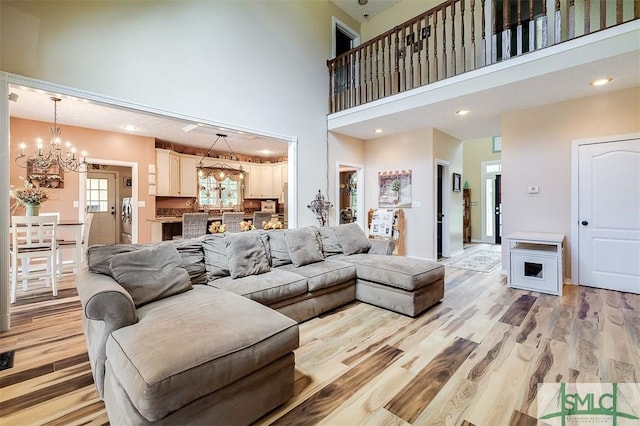 living room with washer / clothes dryer, an inviting chandelier, a towering ceiling, and light wood-type flooring