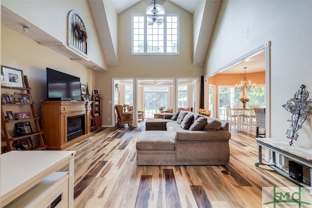 living room featuring light wood-type flooring, a towering ceiling, and ceiling fan with notable chandelier