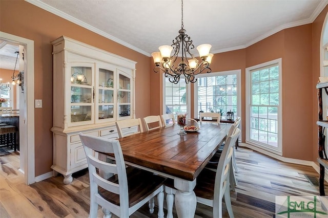 dining area with crown molding, light wood-type flooring, and an inviting chandelier