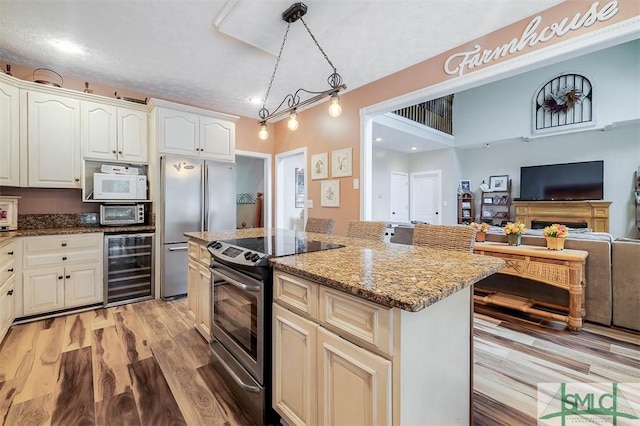 kitchen with hanging light fixtures, wine cooler, light stone counters, a kitchen island, and appliances with stainless steel finishes