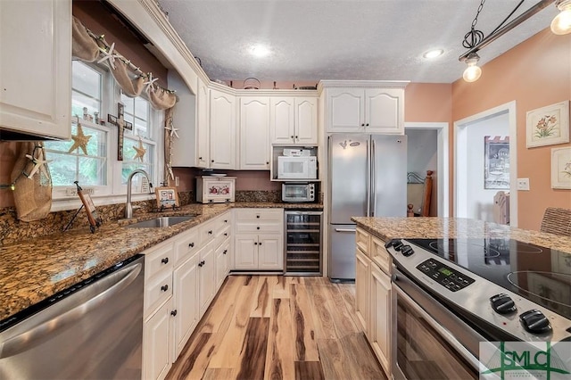 kitchen featuring sink, dark stone countertops, white cabinetry, stainless steel appliances, and beverage cooler