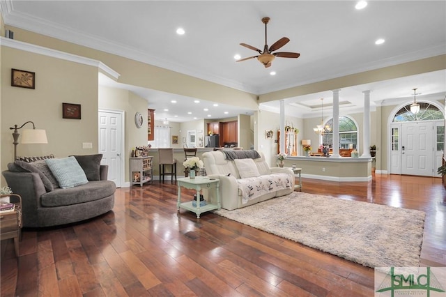 living room featuring crown molding, wood-type flooring, ceiling fan with notable chandelier, and ornate columns