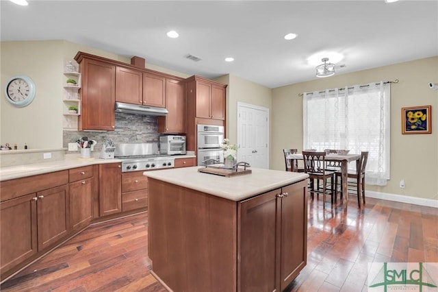 kitchen featuring dark wood-type flooring, sink, appliances with stainless steel finishes, a kitchen island, and decorative backsplash