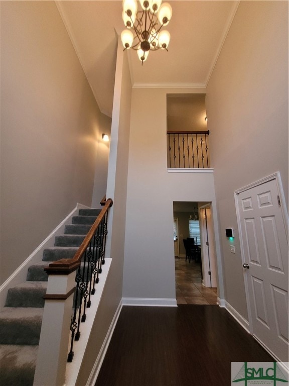 stairs with an inviting chandelier, wood-type flooring, ornamental molding, and a towering ceiling