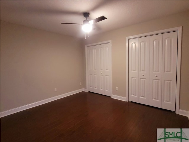 unfurnished bedroom with dark hardwood / wood-style flooring, multiple closets, and ceiling fan