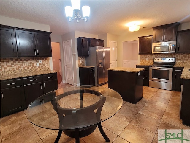 kitchen with a chandelier, a center island, backsplash, appliances with stainless steel finishes, and decorative light fixtures