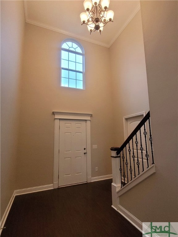 entrance foyer with ornamental molding, an inviting chandelier, a high ceiling, and dark wood-type flooring