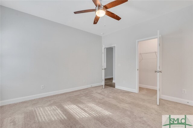 unfurnished bedroom with light carpet, ceiling fan, a walk in closet, and a closet