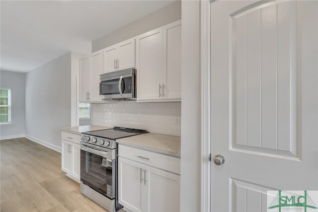 kitchen with white cabinets, light hardwood / wood-style floors, decorative backsplash, and appliances with stainless steel finishes