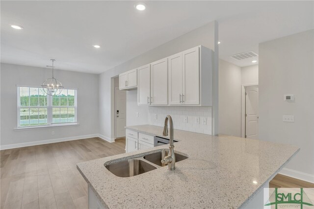 kitchen with white cabinets, sink, light stone countertops, light hardwood / wood-style flooring, and decorative light fixtures